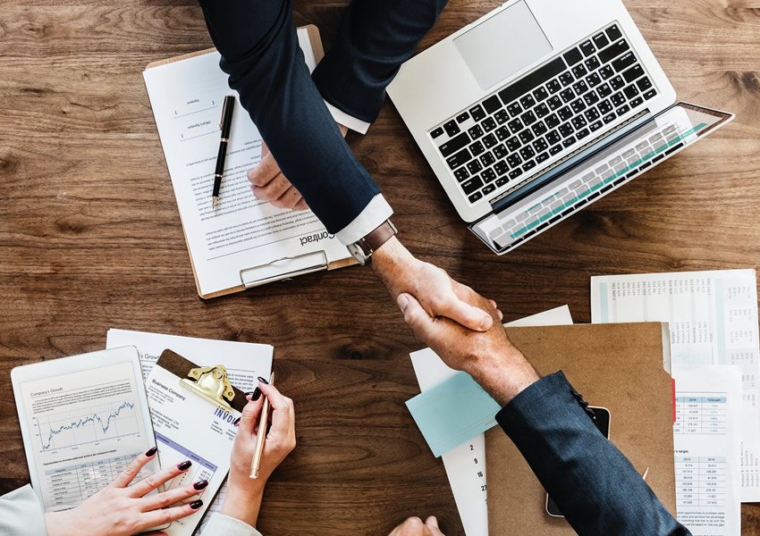 Handshake over a computer signifying successful agreement; BSc in Business Law at GBU-Europe